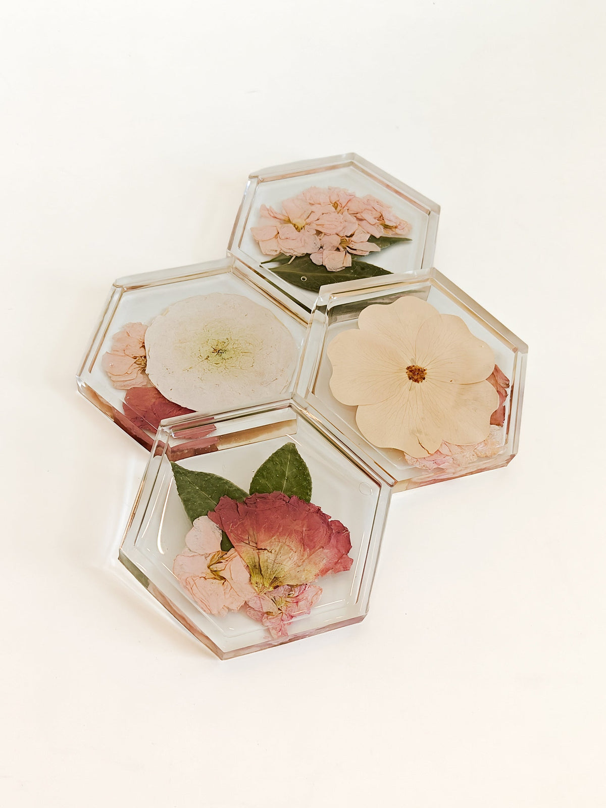 Four hexagonal clear resin coasters with pressed flowers, arranged on a plain white background.