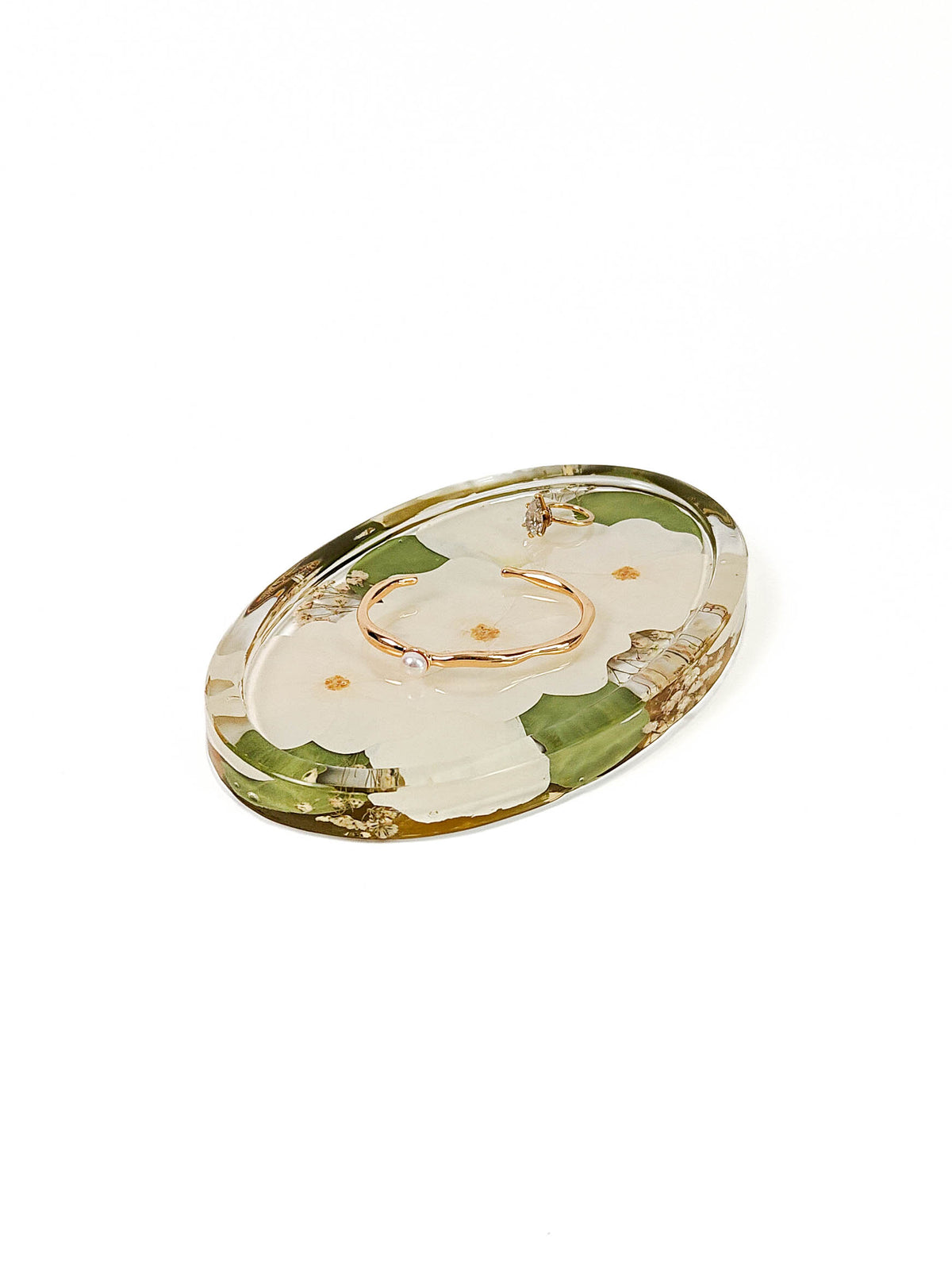An oval resin jewelry organizer tray with a floral pattern in green and cream, featuring a rose gold ring holder in the center, shown on a white background.
