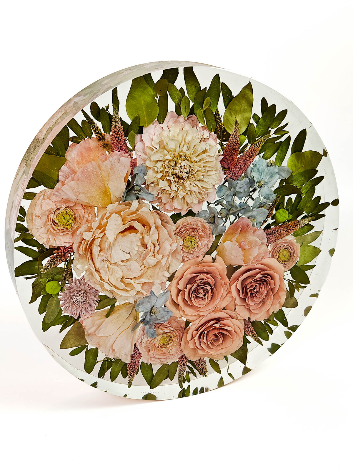 A round glass decorative piece featuring a pressed floral bouquet with peach and cream flowers, green leaves, and small blue accents, displayed on a white background.