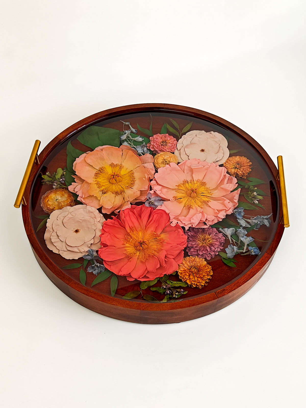 An oval wooden serving tray with gold-toned side handles, decorated with a pressed floral arrangement featuring large peach, coral, and pink flowers with green leaves, photographed on a clean white background.