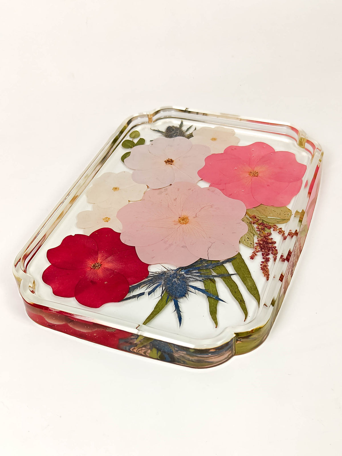 A rectangular clear resin tray with rounded corners, filled with pressed flowers including pink, red, and white blossoms with green leaves, photographed on a plain white background.
