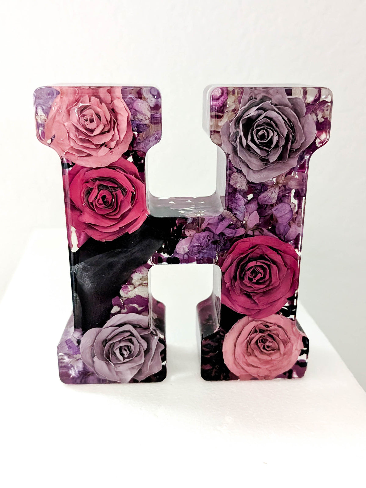A decorative resin letter H featuring a floral print of pink and purple roses, displayed on a white surface against a white background.