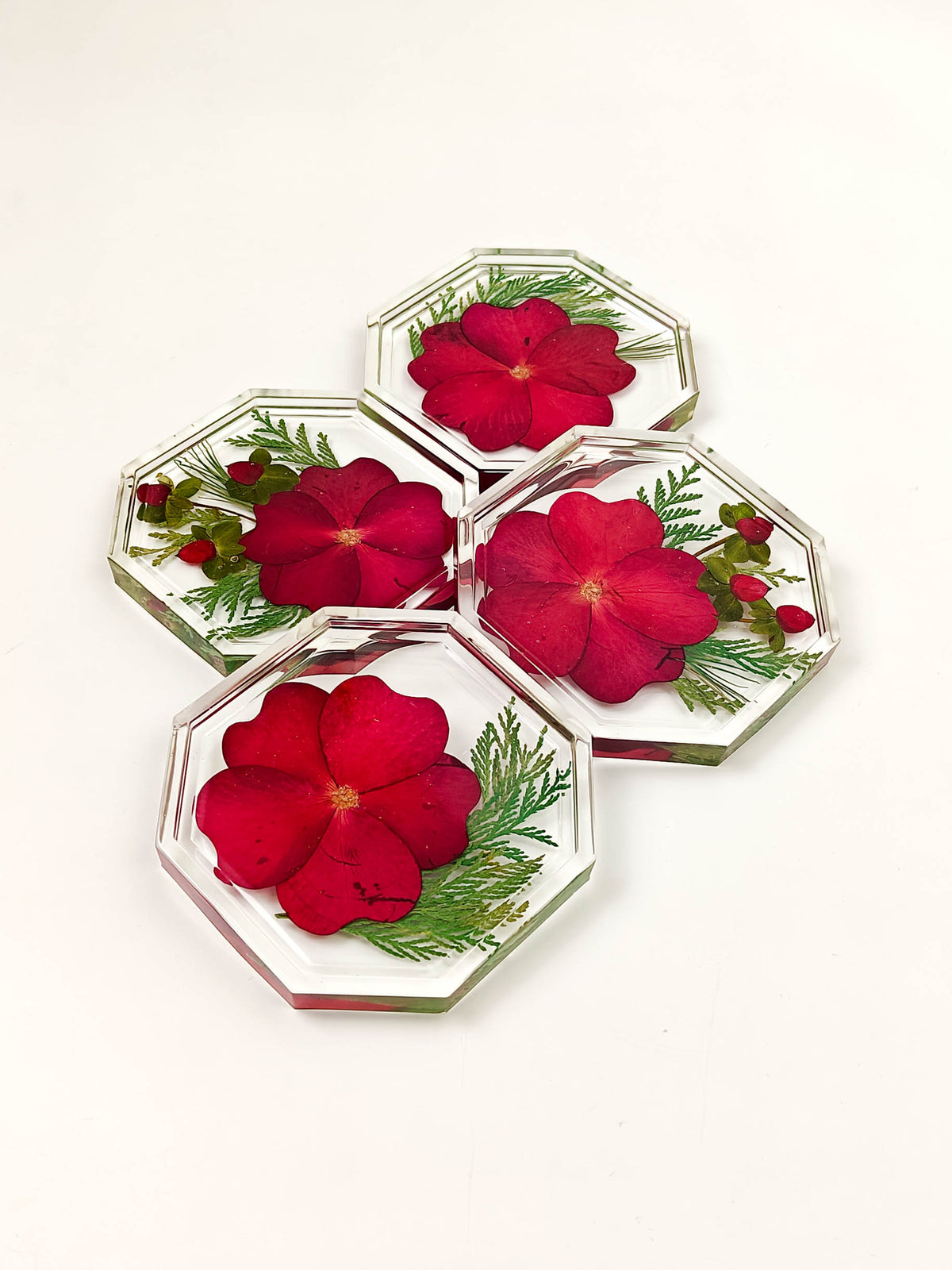 Four octagonal clear resin coasters with embedded red flowers and green leaves, arranged on a plain white background.