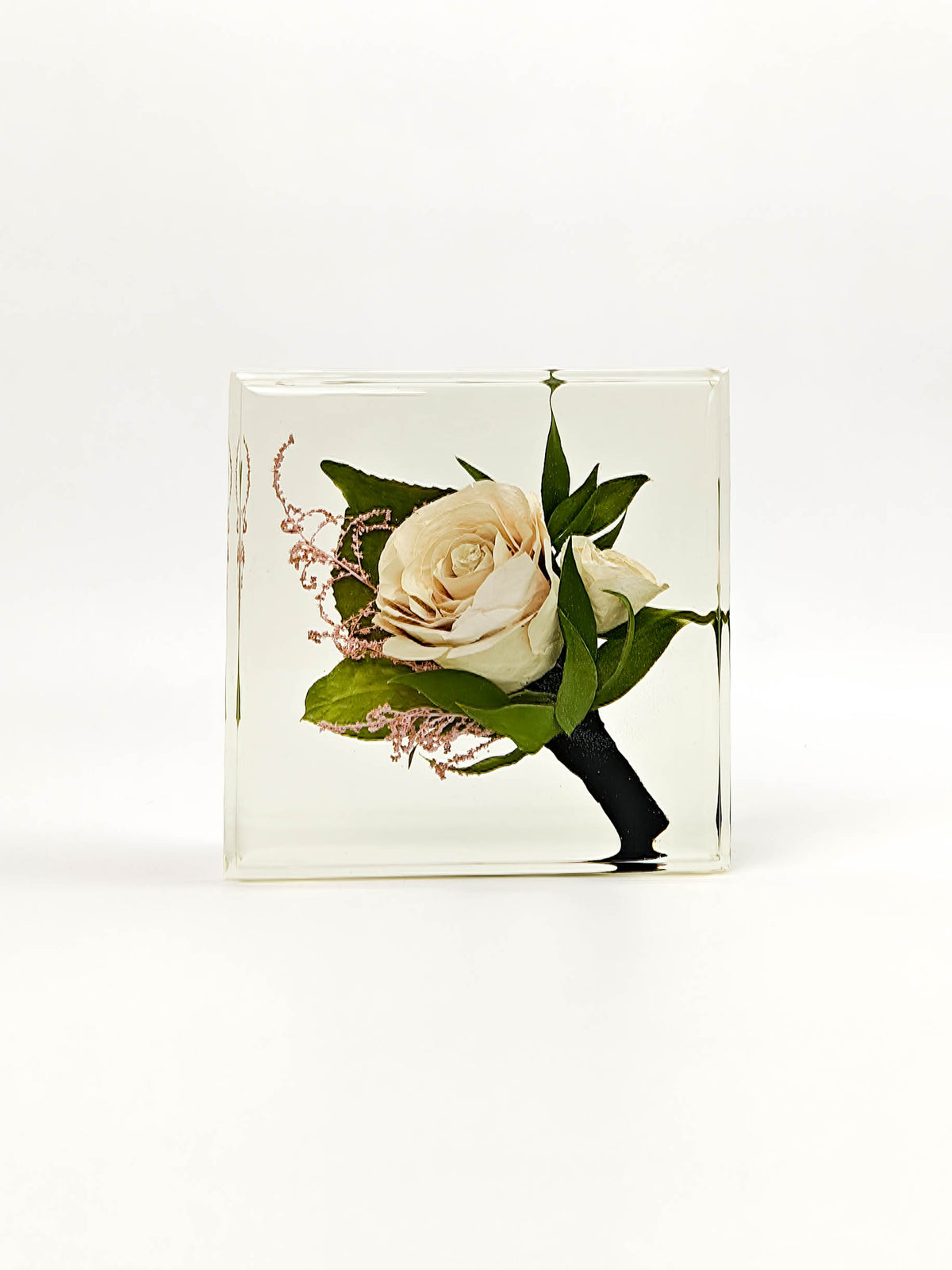 A square clear resin keepsake block containing a pressed floral arrangement with a cream rose, green leaves, and small pink sprigs, shown on a clean white background.