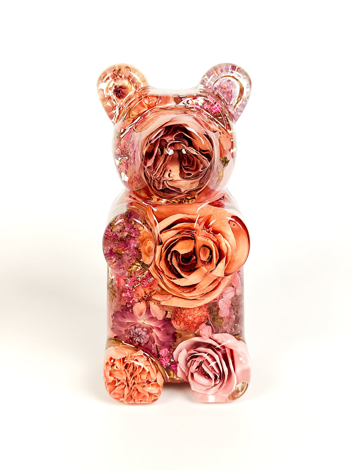 A clear resin teddy bear figurine filled with dried pink and peach roses, set against a plain white background.