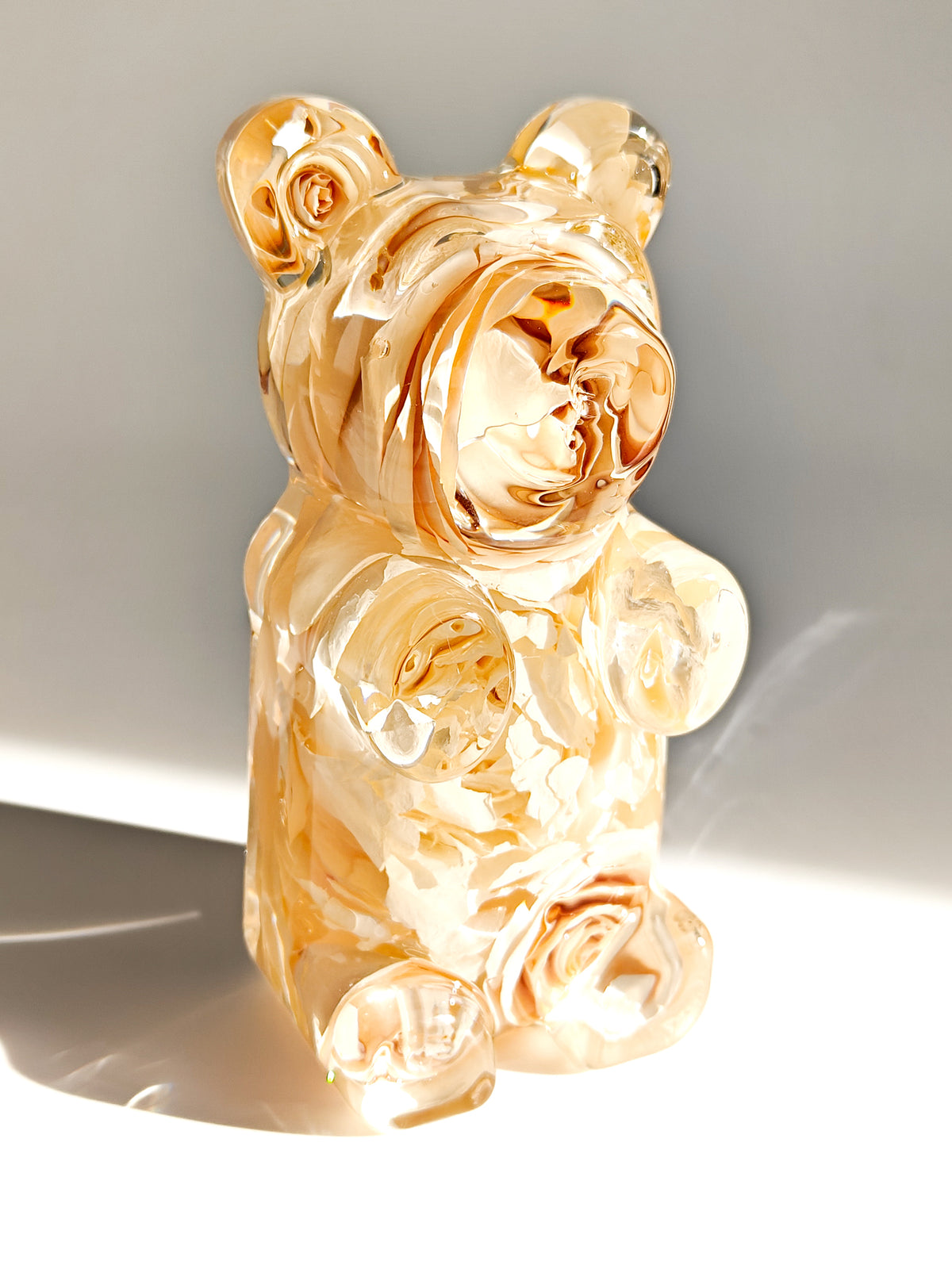 A translucent amber-colored glass bear figurine with a glossy, marbled finish, standing on a white surface against a neutral gray background with soft shadows.