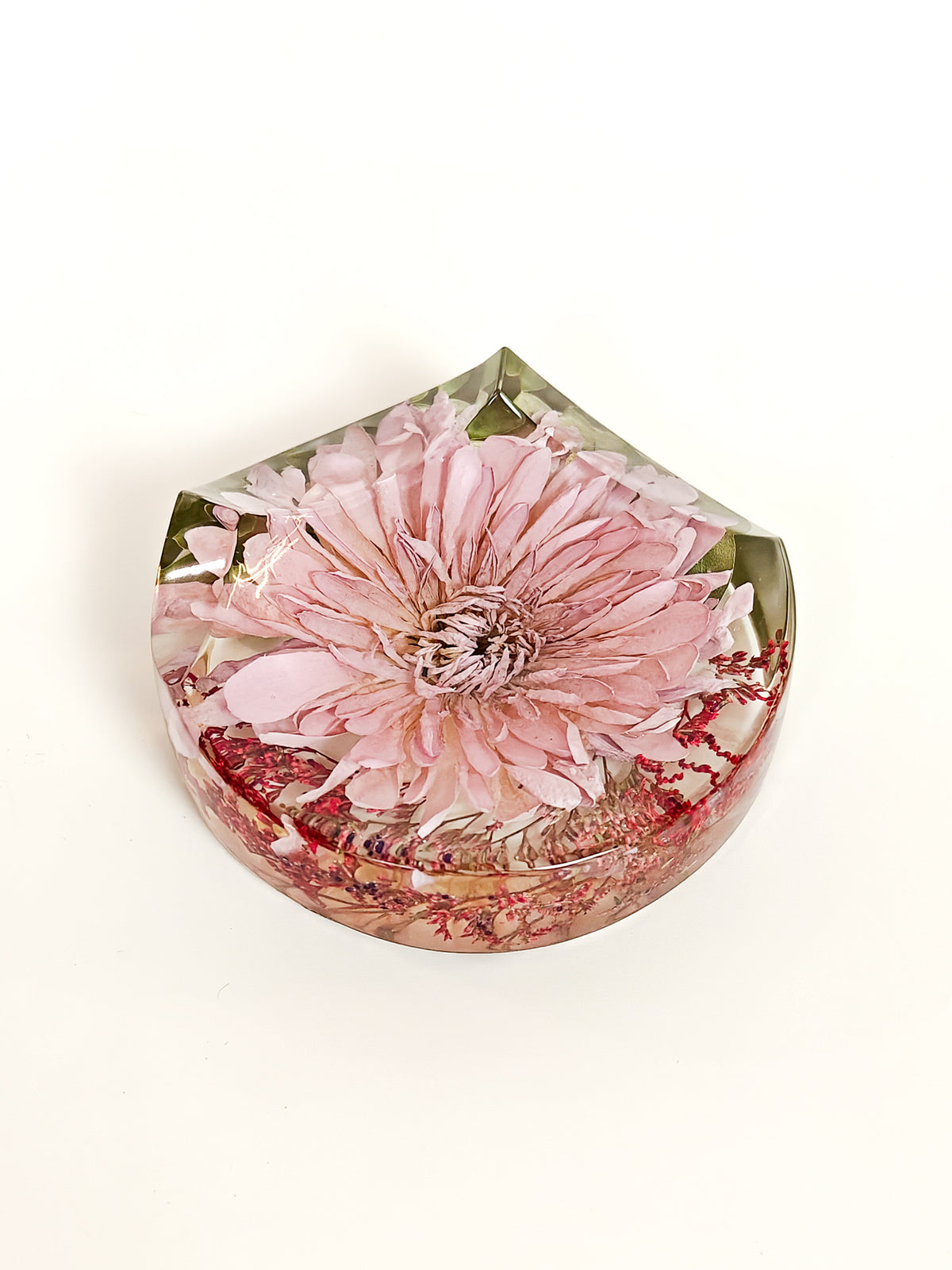 A faceted clear resin keepsake or decorative piece featuring a preserved pink flower and red botanical inclusions, photographed on a clean white background.