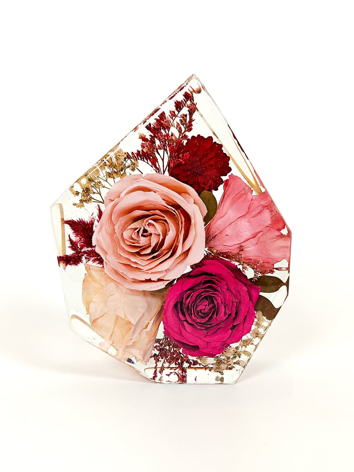 A clear resin geometric vase containing a preserved dried flower arrangement with pink and red roses, photographed on a white background.