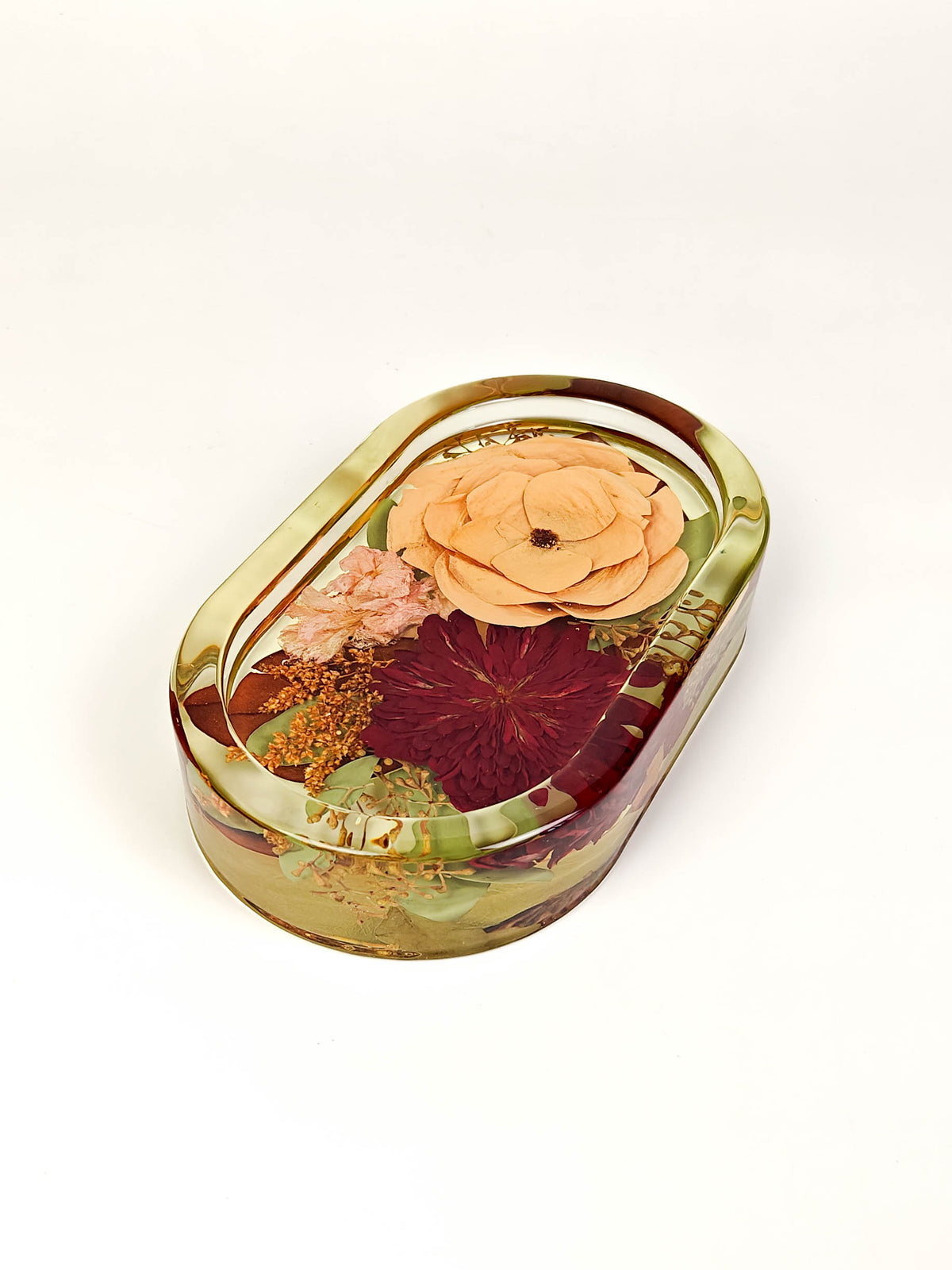 An oval resin keepsake box with a gold-toned rim, filled with dried flowers and botanical elements, photographed on a clean white background.