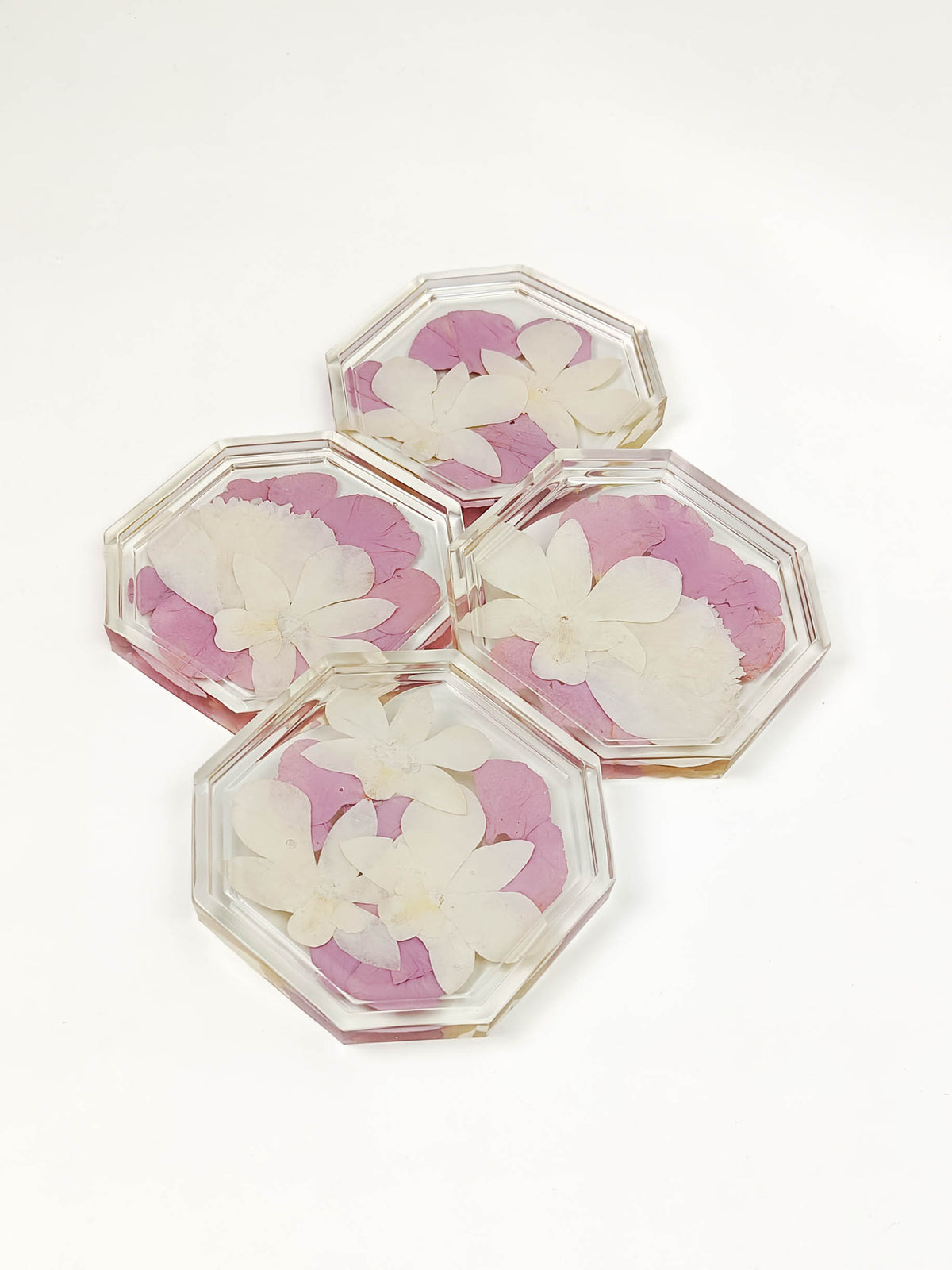Four clear octagonal resin coasters with pressed white flowers and pink petals, arranged on a plain white background.