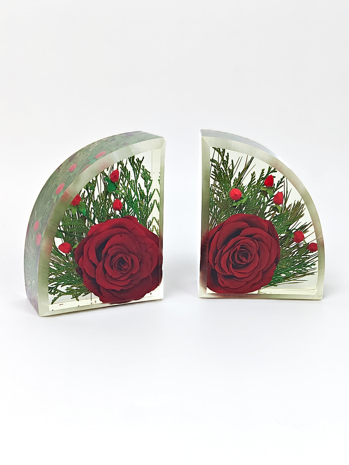 Two arched clear resin blocks, each featuring a large red rose, green pine needles, and small red berries, displayed on a light gray background.