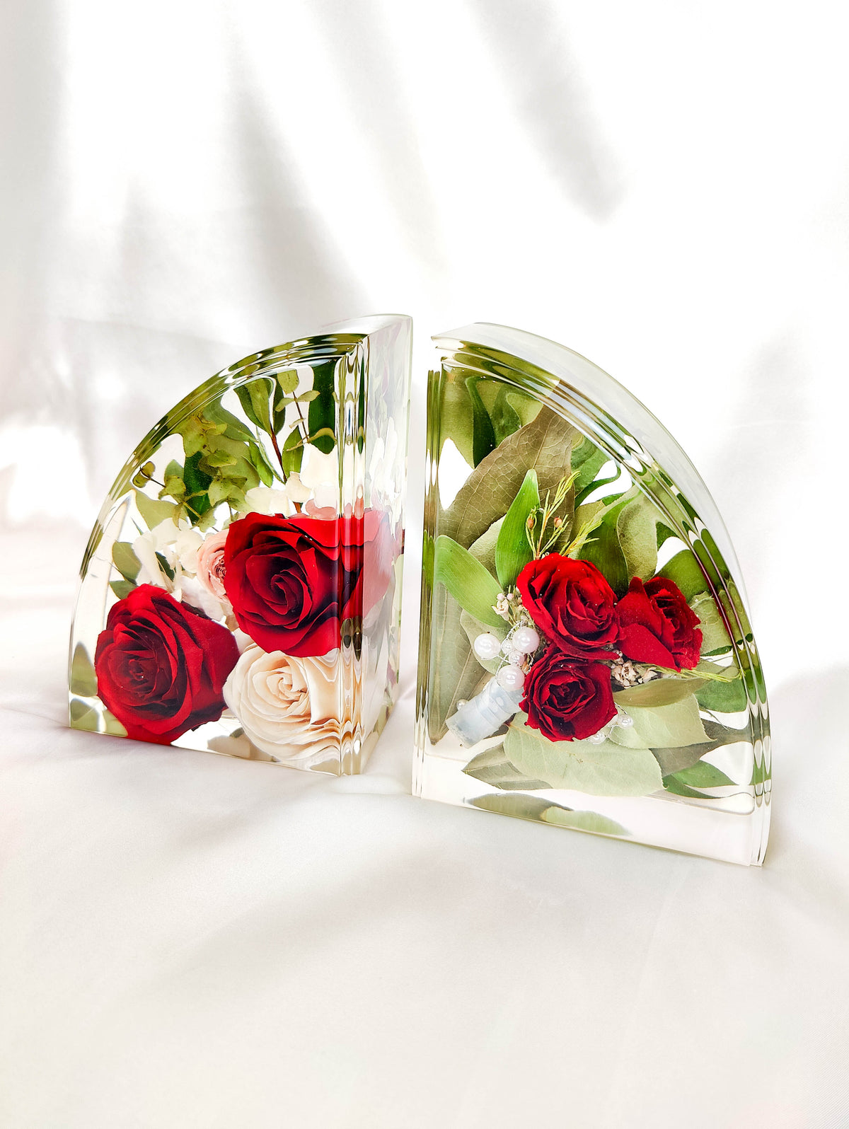 Two clear acrylic wall art pieces shaped like semi-circles, each containing a floral arrangement with red and cream roses and green leaves, displayed on a white surface against a white background.