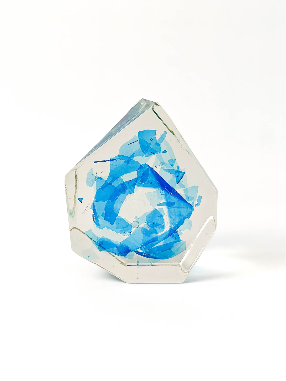 A faceted clear resin or glass-like decorative object with layered translucent blue abstract shapes inside, photographed on a clean white background.