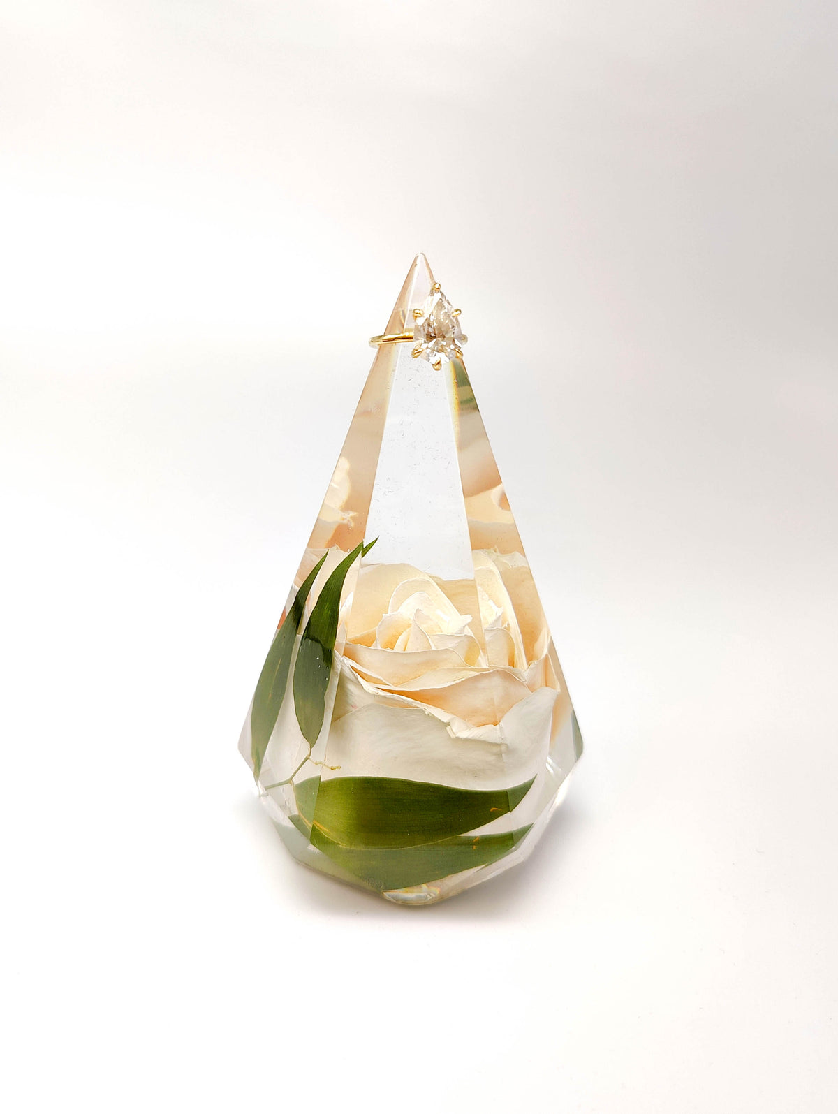 A faceted crystal-like keepsake urn containing a preserved white rose with green leaves, set against a clean white background.