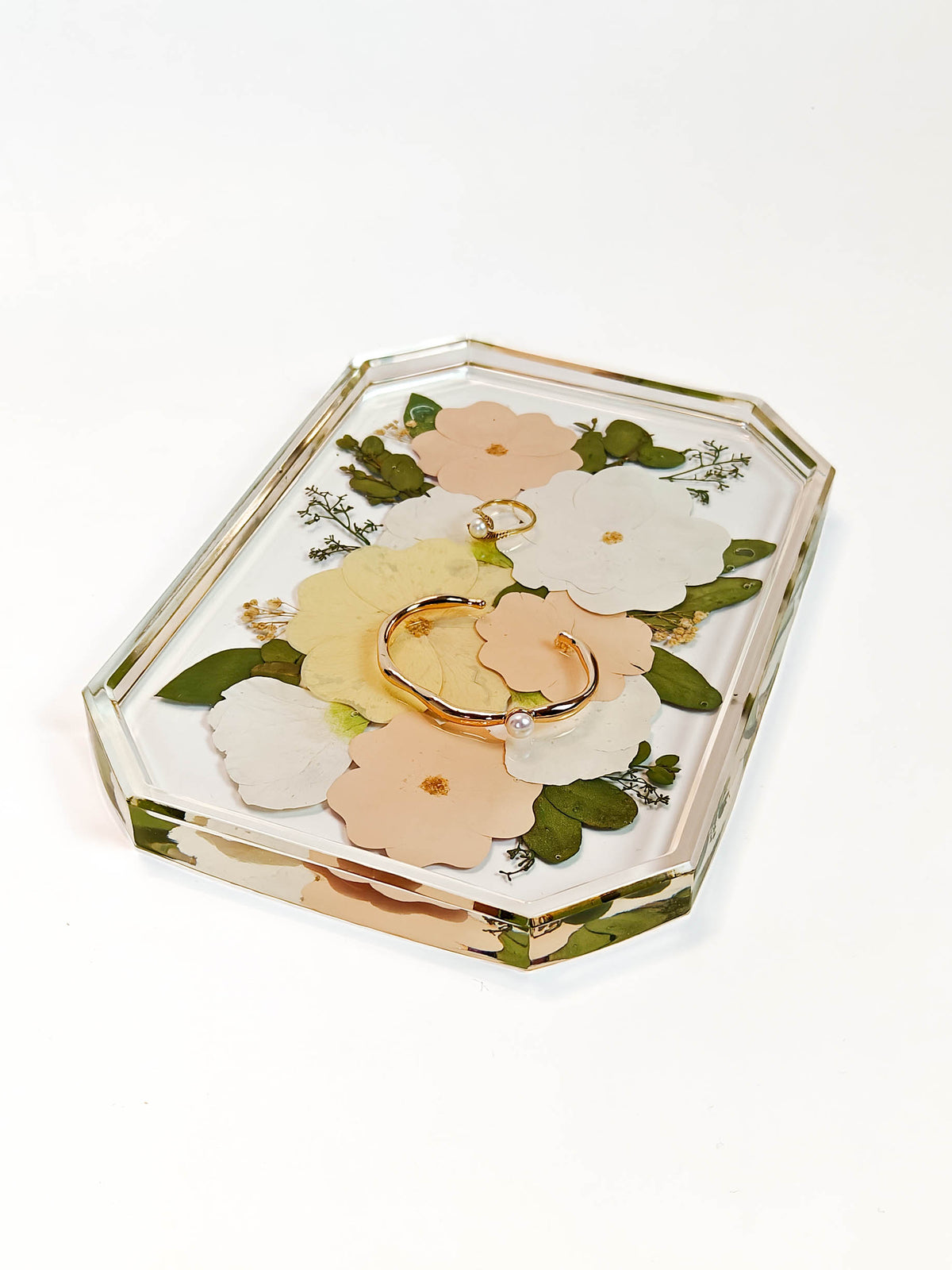 A clear acrylic ring box with a floral design, featuring pressed-style peach, white, and yellow flowers with green leaves, containing a gold ring, on a white background.